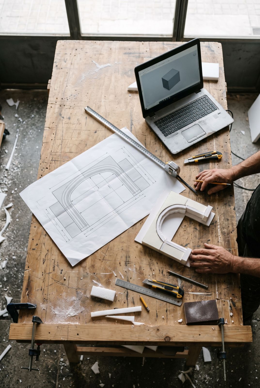 Plano de un arco dividido en módulos, maqueta de poliespán y portátil con modelo 3D
